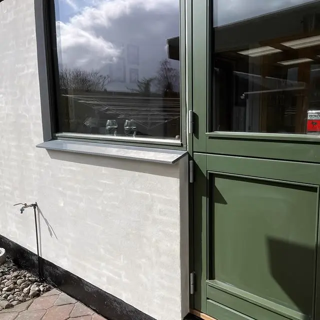 Facade med hvid kalkpuds og grøn snedkerdetalje på vindue og dør